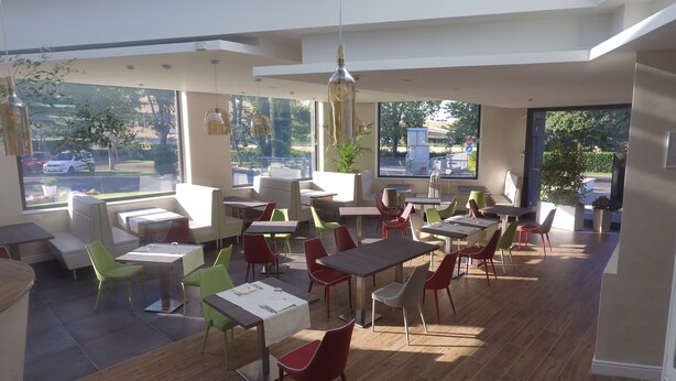 A modern restaurant with a mix of booth and table seating, large windows offering views of the street, and a variety of colorful chairs.