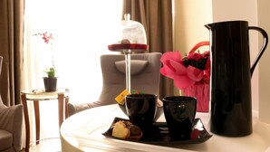 A cozy hotel room with a dining table set for breakfast, including pastries and a coffee pot.