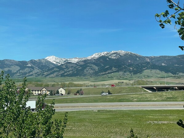 A rural landscape with a mountain range in the background, a road with vehicles, and buildings in the foreground. - Country Inn & Suites by Radisson, Bozeman, MT (Bozeman)