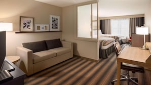 A hotel room with a sofa, a desk, a bed, and a large window.