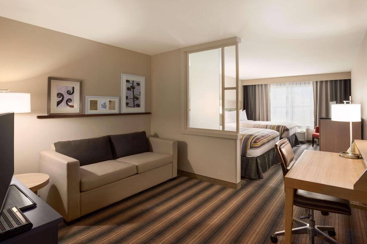 A hotel room with a sofa, a desk, a bed, and a large window.