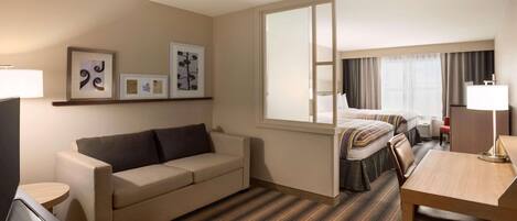 A hotel room with a sofa, a desk, a bed, and a large window.