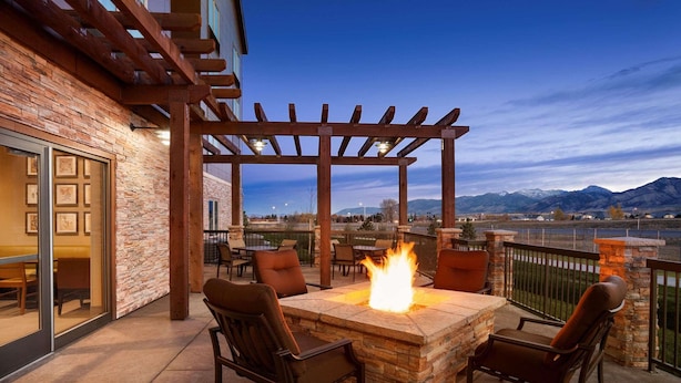 An outdoor patio with a stone fire table, two chairs, and a pergola.