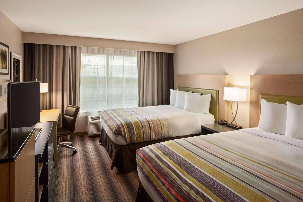 A hotel room with two beds, a desk, a chair, a TV, and a window with curtains.