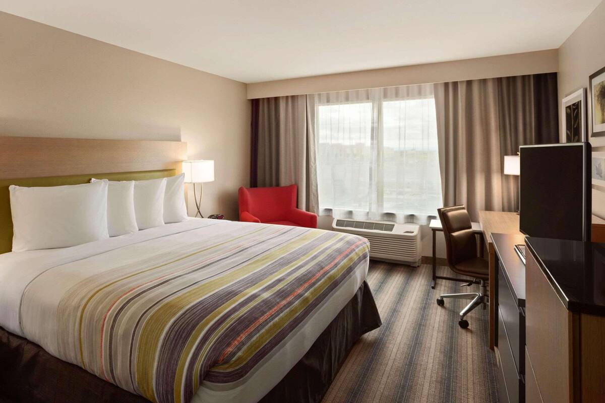 A hotel room with a large bed, a desk with a chair, a TV, and a window with curtains.