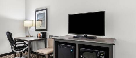 Quarto de hotel com escrivaninha, cadeira, televisão, micro-ondas e pequeno frigorífico.
