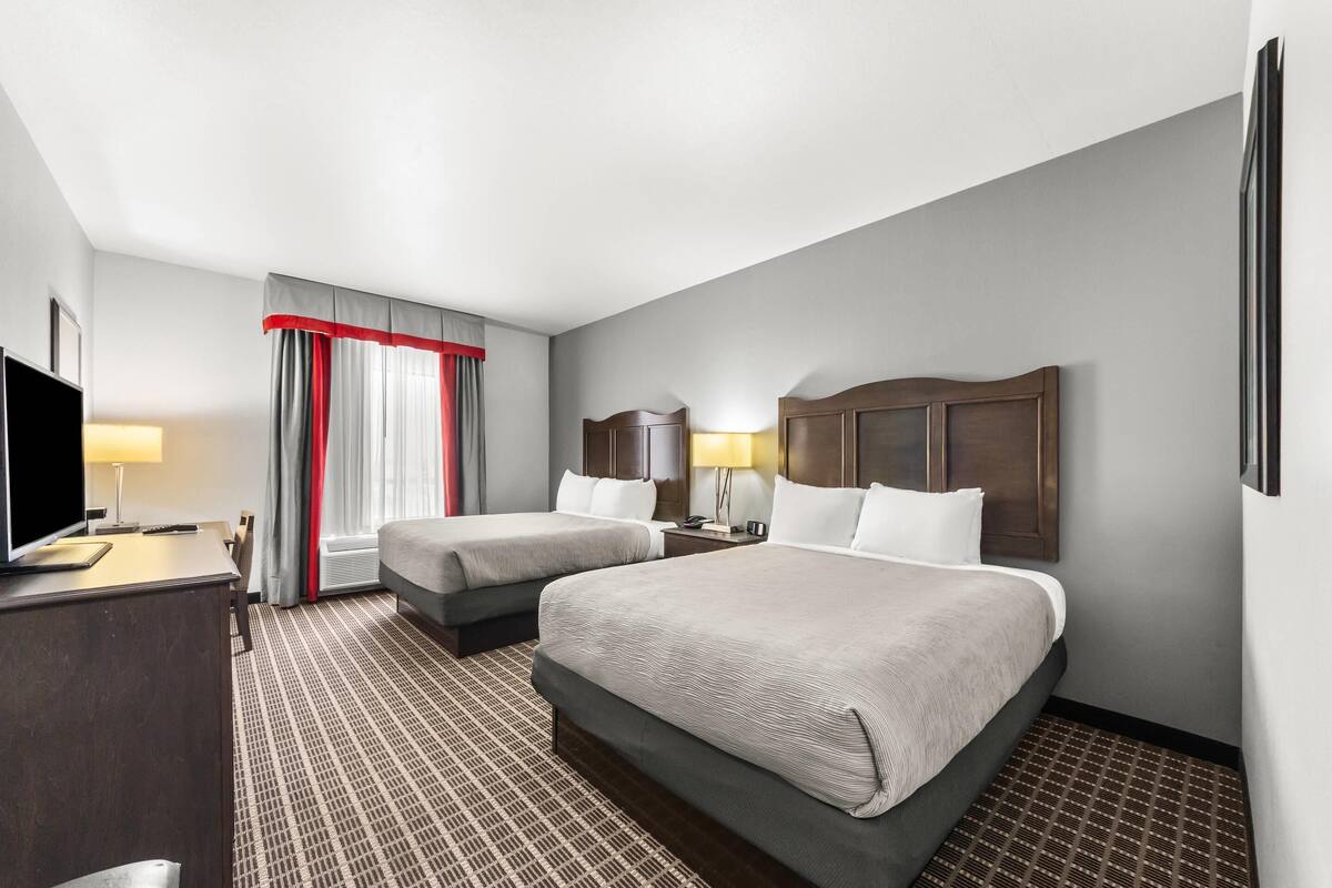 Une chambre d’hôtel avec deux lits, une télévision, un bureau et une fenêtre avec des rideaux.