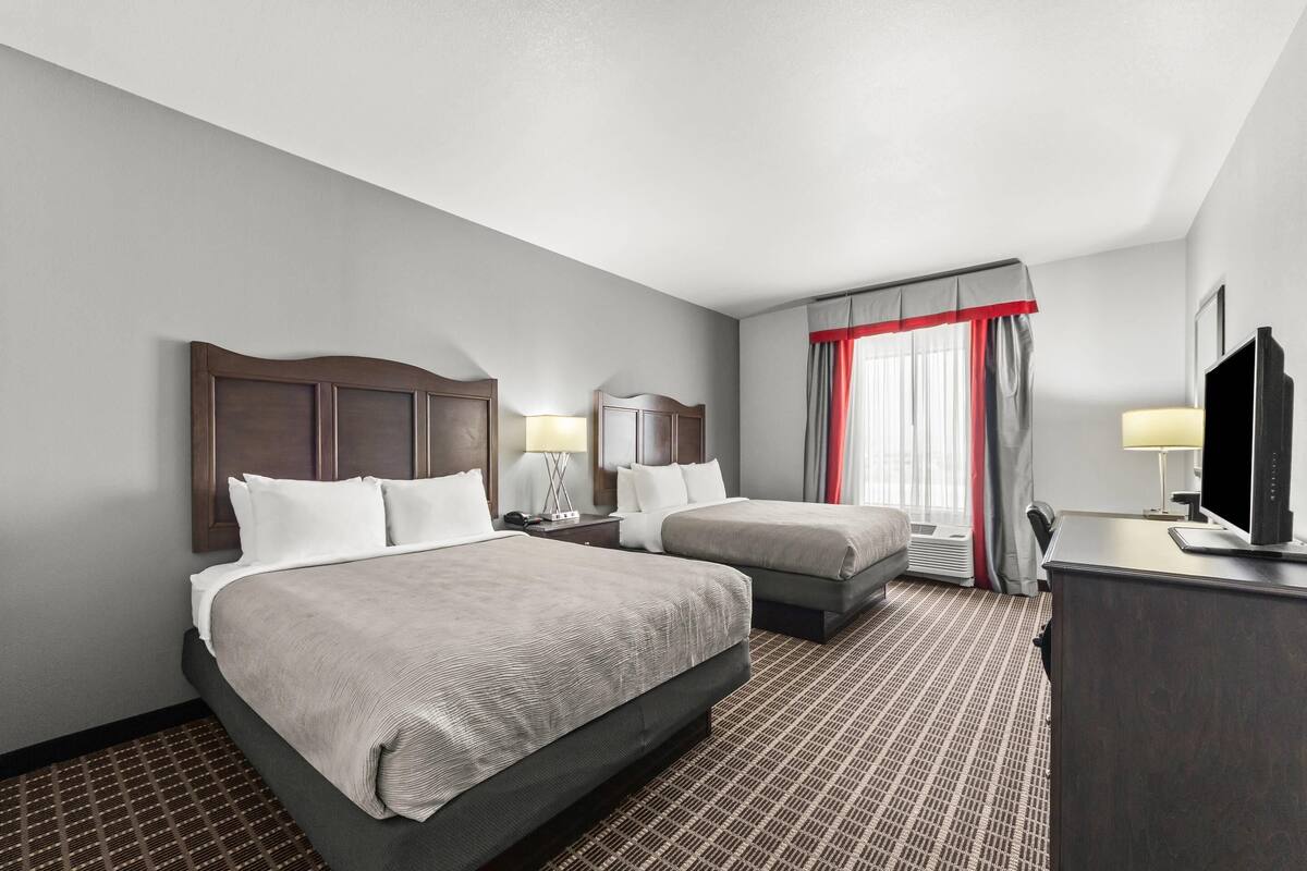 Une chambre d’hôtel avec deux lits, un bureau, une télévision et une fenêtre avec des rideaux.