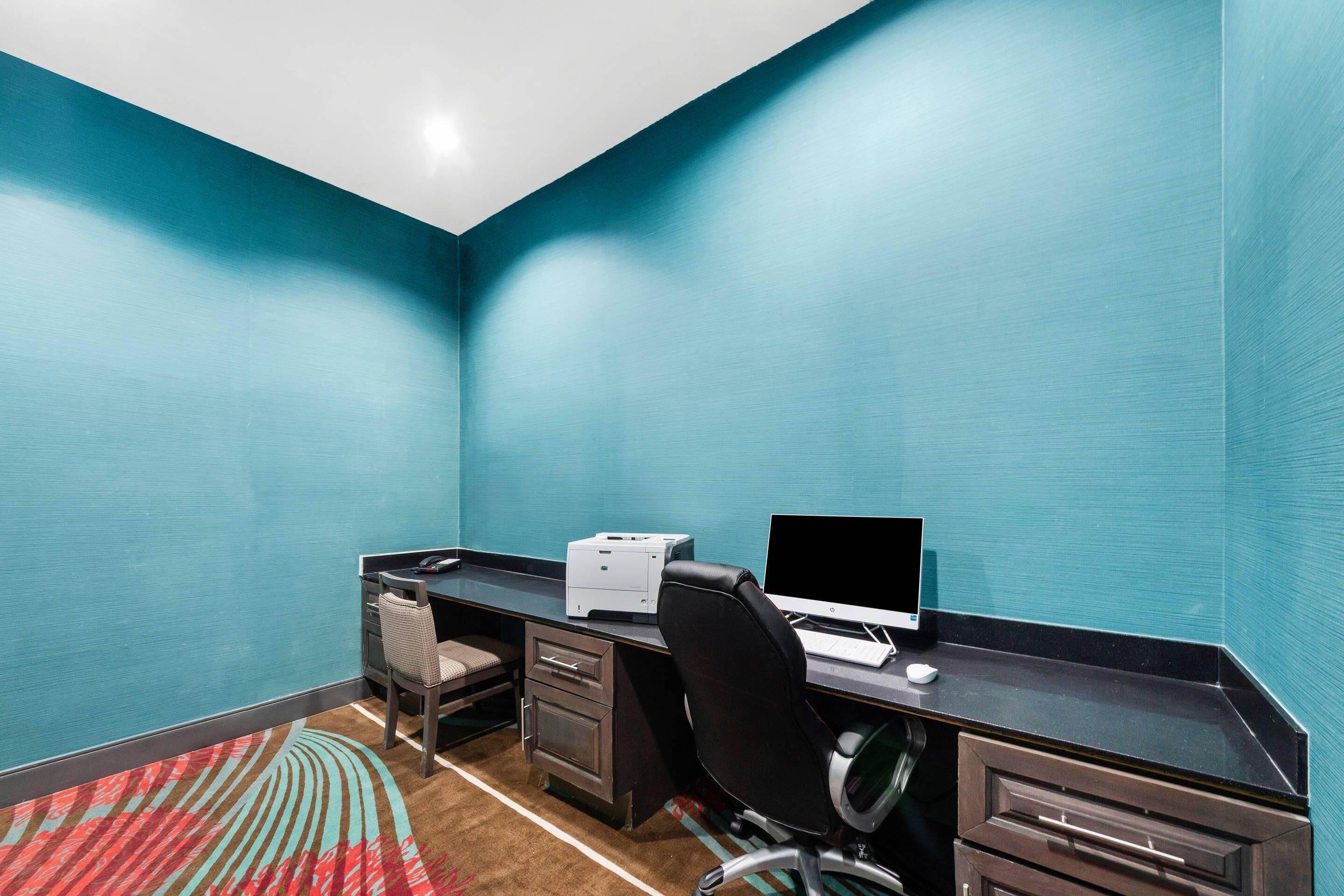 A room with teal walls, a desk with a computer, a printer, and a chair.