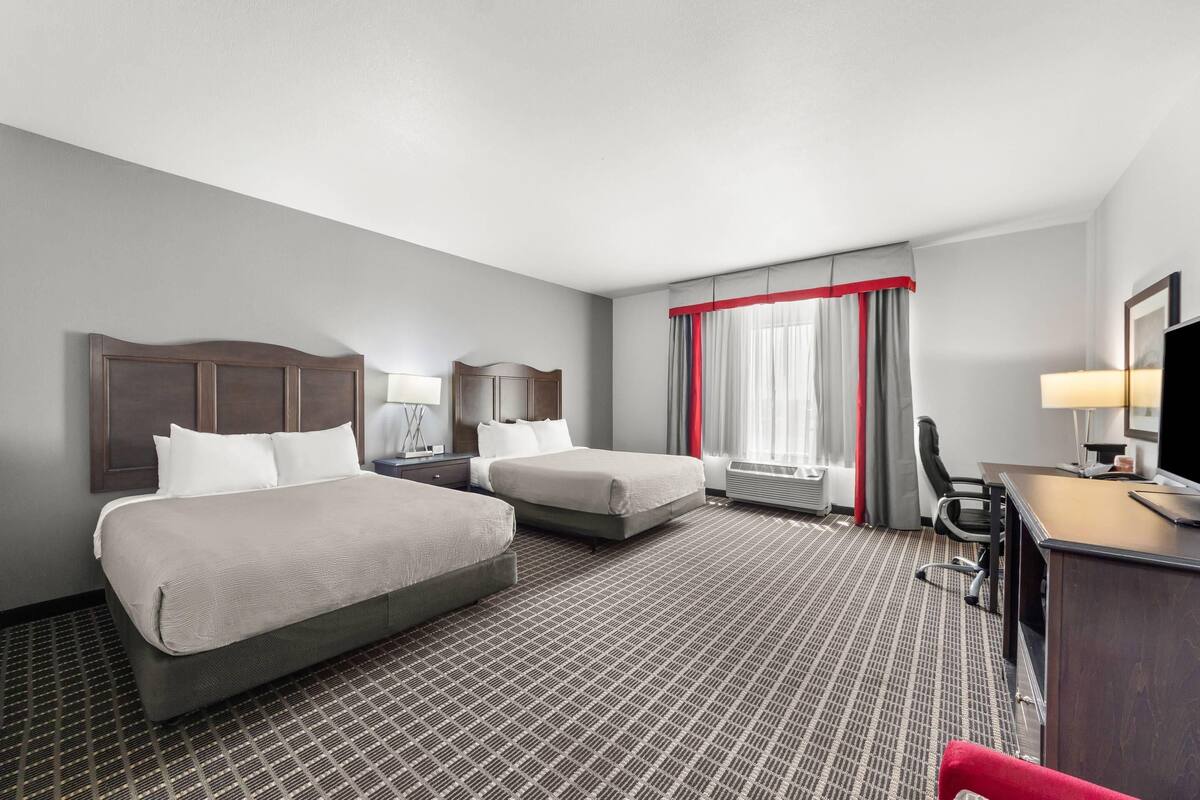 Une chambre d’hôtel avec deux lits, un bureau, une chaise et un téléviseur.