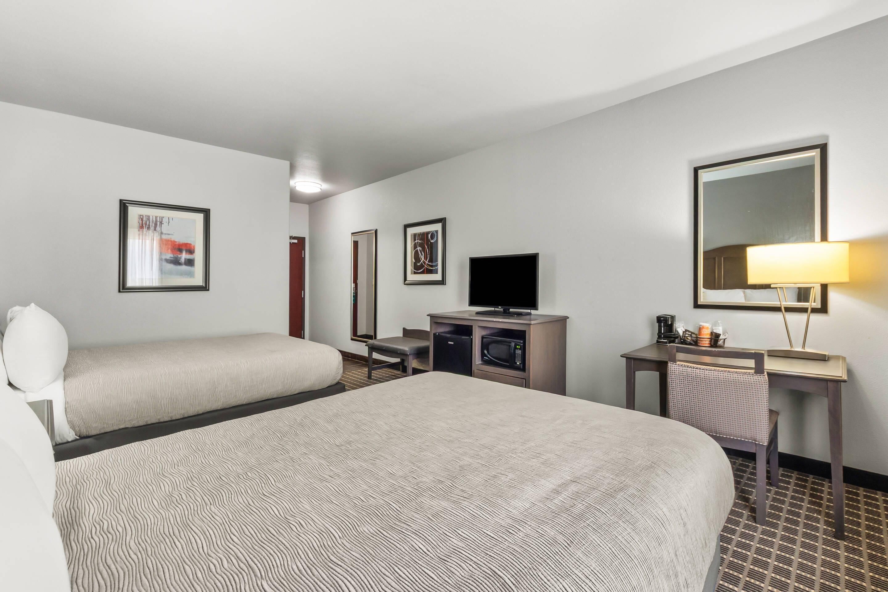A hotel room with two beds, a desk with a television, a microwave, and a lamp.