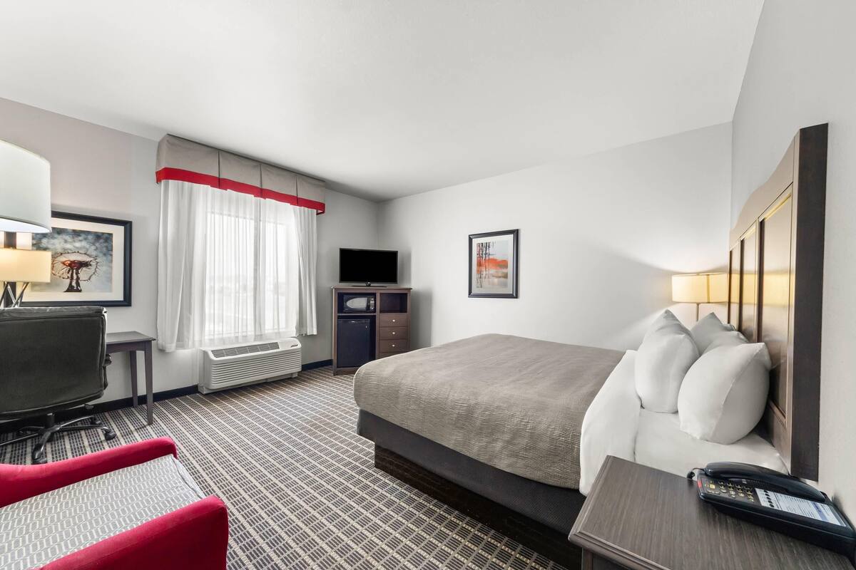 Une chambre d’hôtel avec un lit, un bureau, une chaise, une télévision et une fenêtre avec des rideaux.
