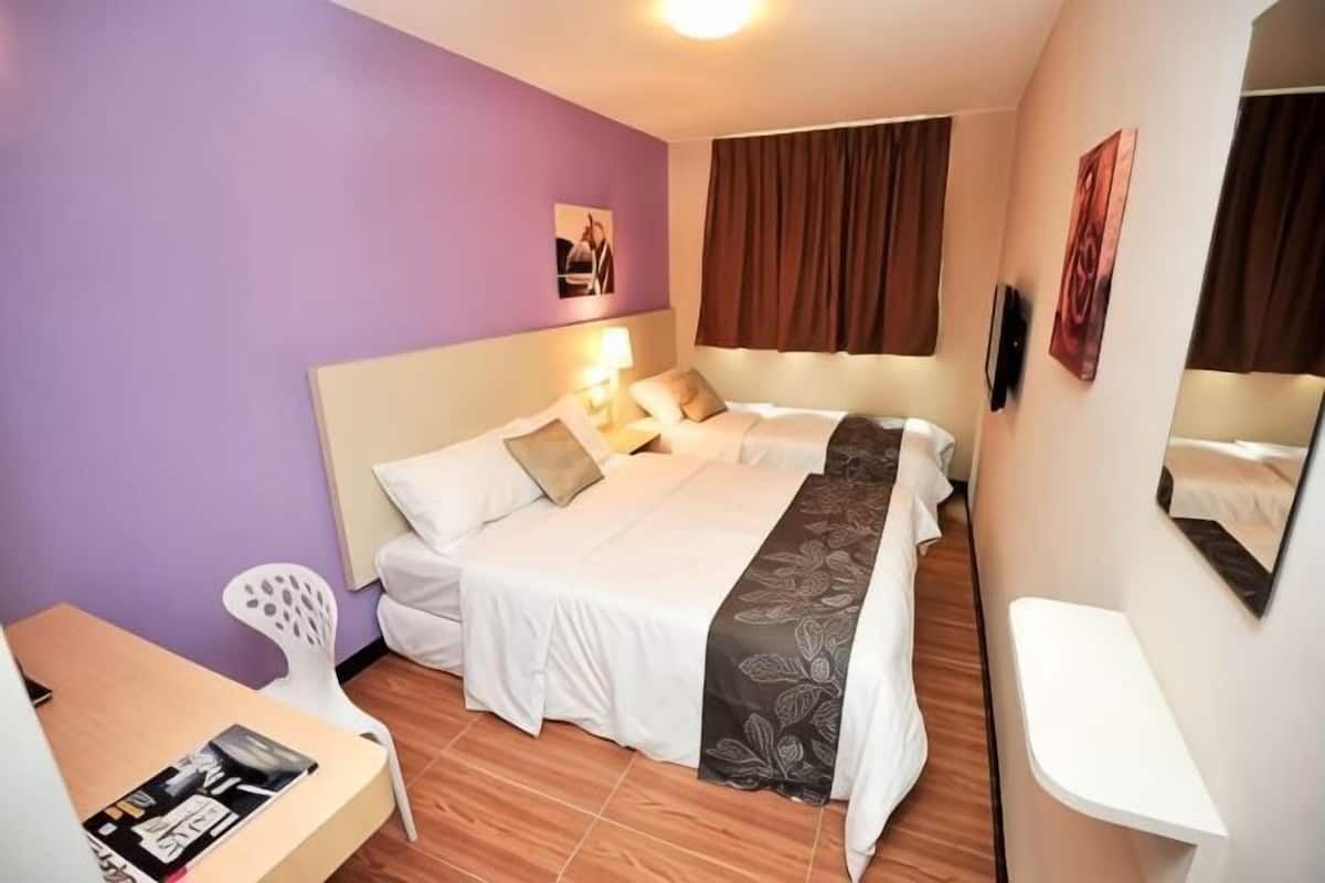 A hotel room with a bed, bedside table, chair, and a desk.