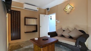 A room with a sofa, a small wooden table, an air conditioning unit, a door, and a wall-mounted shelf. - At Smile Oasis Houses (Bangkok)