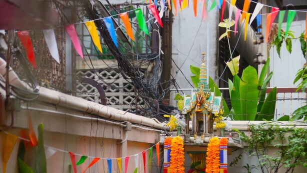 A courtyard with potted plants, a small shrine, and colorful flags. - At Smile Oasis Houses (Bangkok)