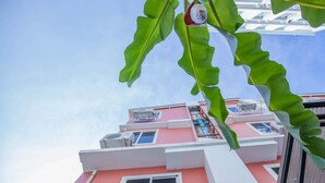 A pink building with multiple windows and balconies, viewed from below through green foliage. - At Smile Oasis Houses (Bangkok)
