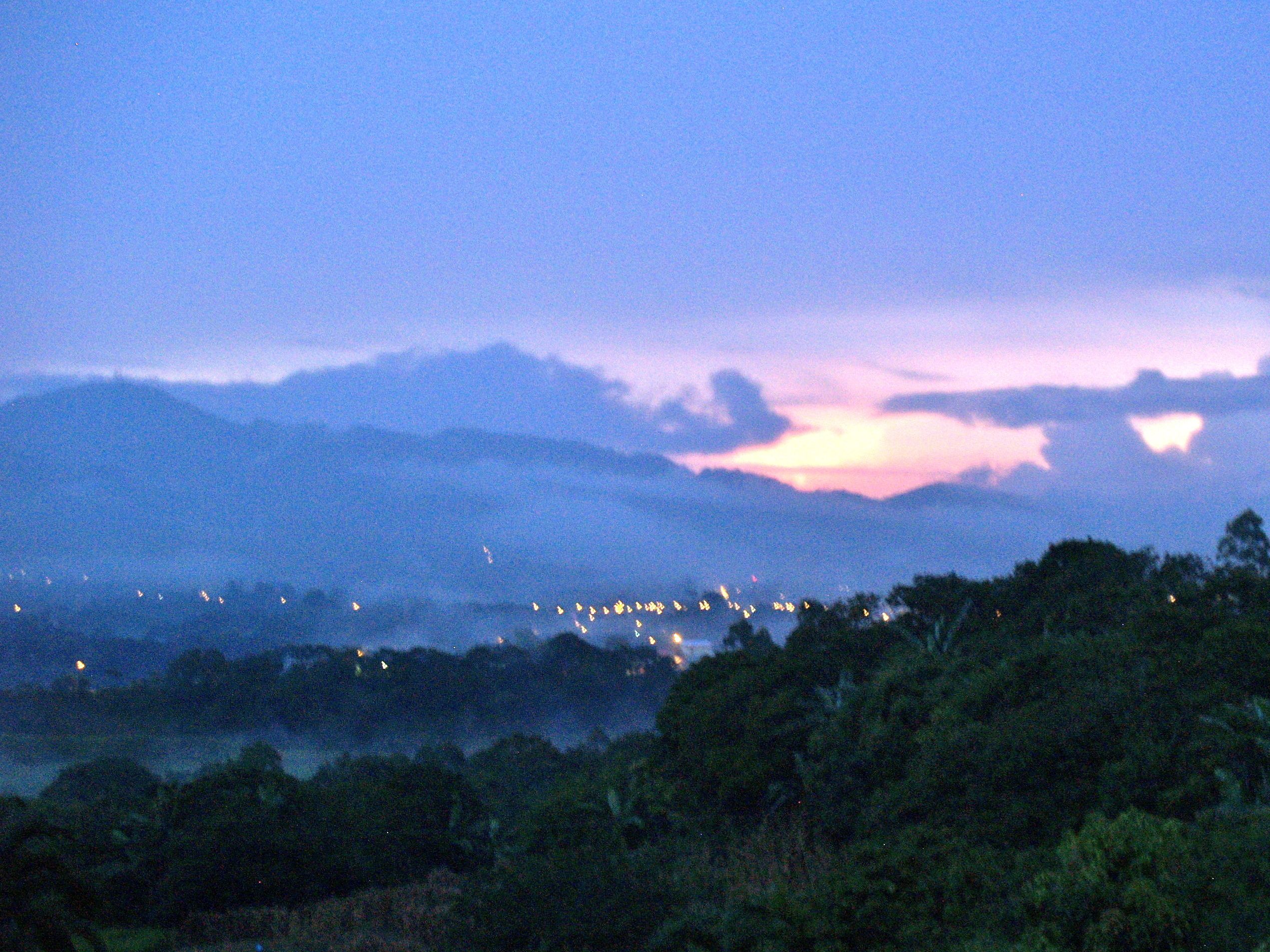 A mountainous landscape at dusk with a city in the valley.