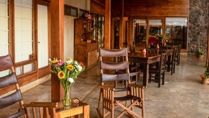 A spacious indoor area with wooden furniture, including chairs and a table, and a stone wall in the background. - Casa Amanecer Bed & Breakfast (San Juan)
