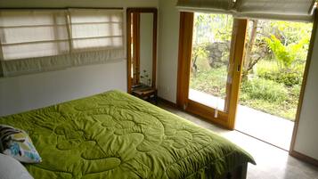 Ein Schlafzimmer mit Bett, Spiegel, Fenster mit Blick auf Grünflächen und einer zur Außenseite führenden Tür.