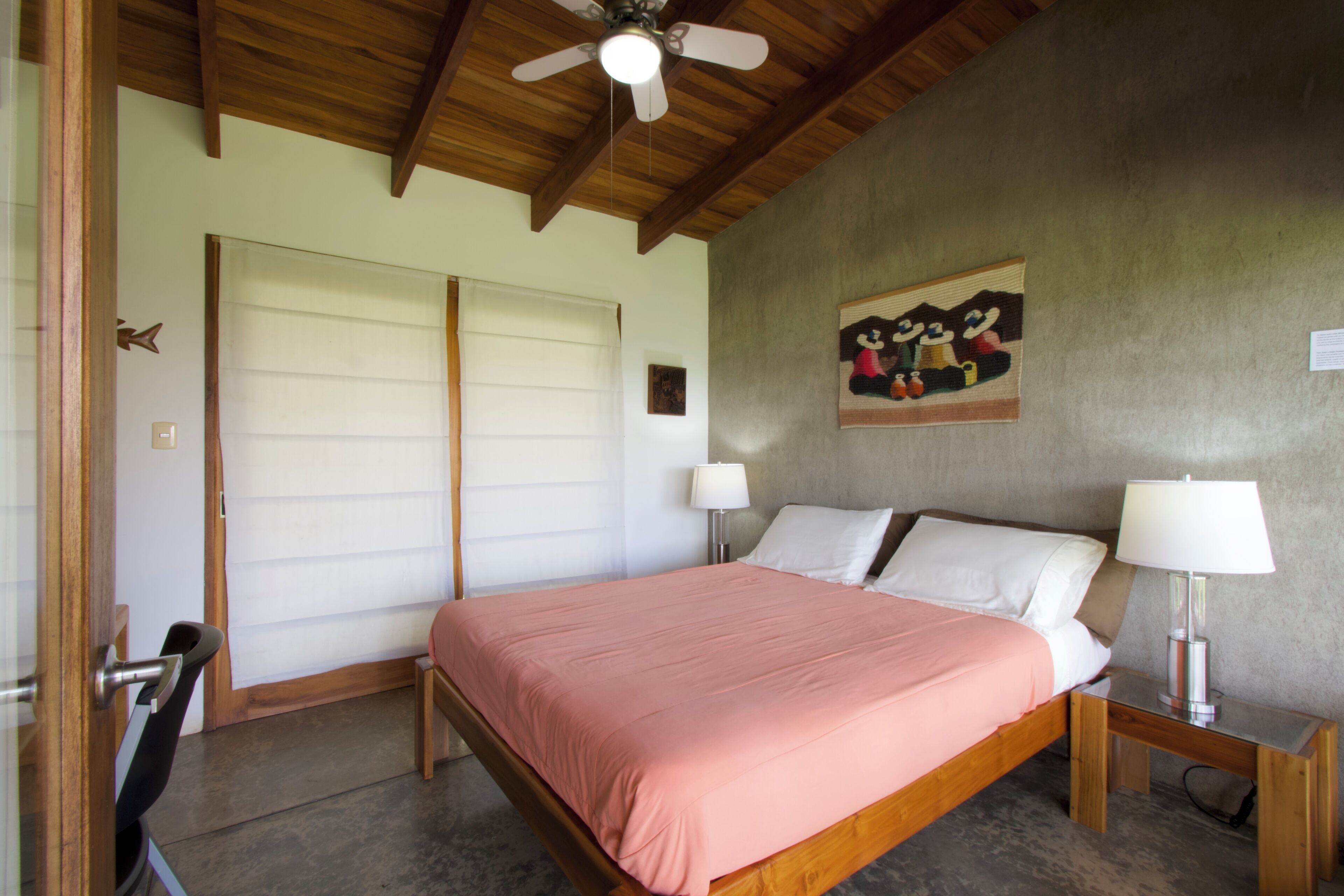 A bedroom with a wooden bed, a ceiling fan, a nightstand with a lamp, and a painting on the wall.