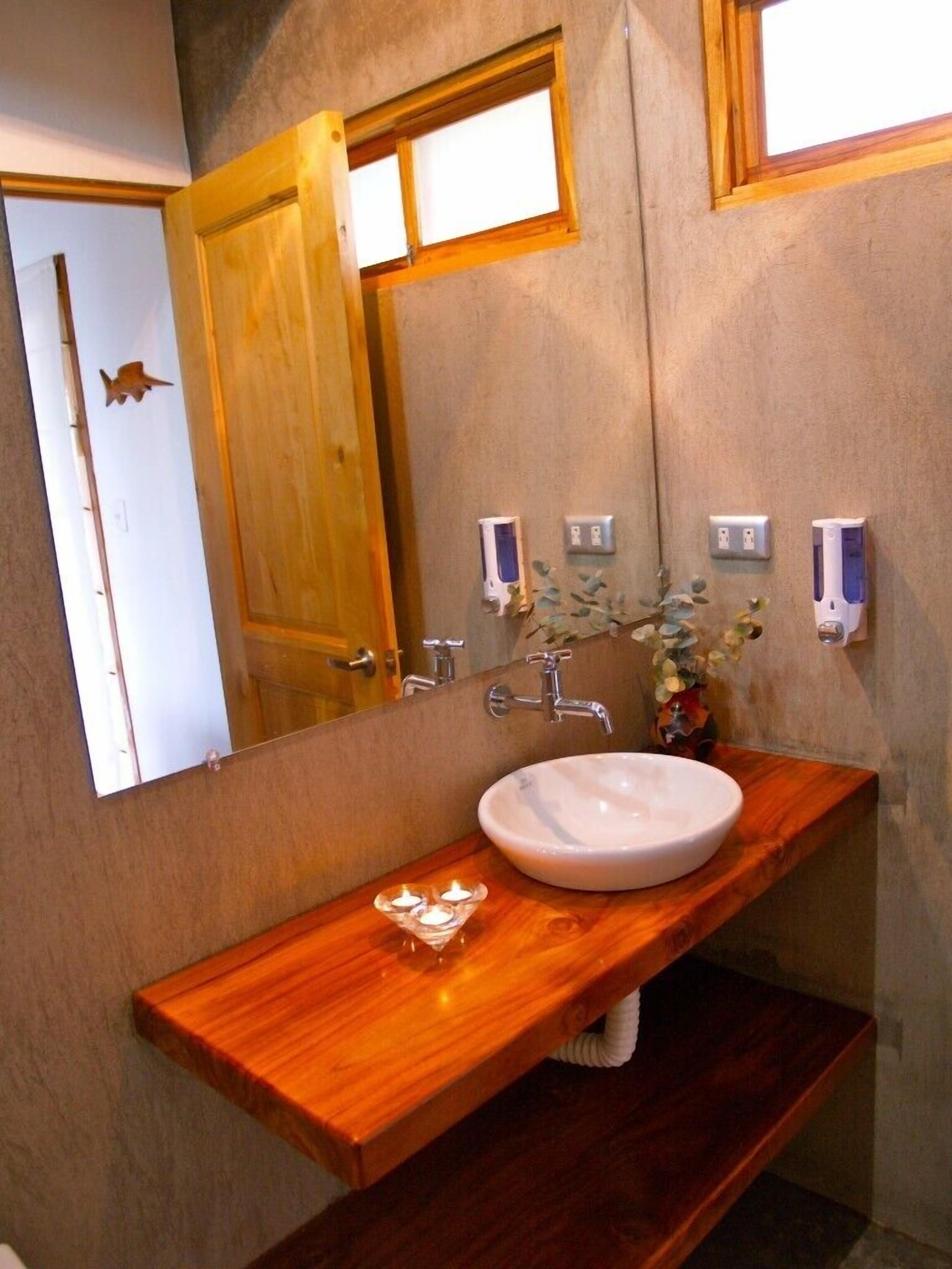 A bathroom with a wooden vanity, a white sink, a mirror, and a window.