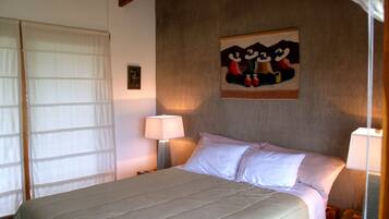 A bedroom with a bed, a nightstand, a lamp, a painting on the wall, and a window with curtains.