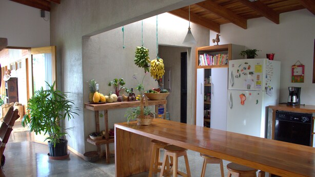 A kitchen with a wooden bar, stools, a refrigerator with magnets, and hanging plants. - Casa Amanecer Bed & Breakfast (San Juan)