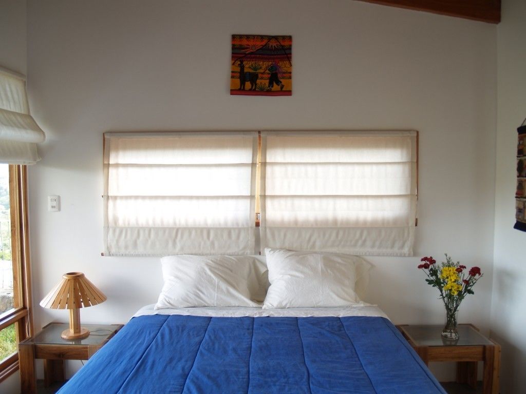 Une chambre à coucher comprenant un lit, une table de chevet, une lampe, une fenêtre avec des stores et un élément de décoration murale.