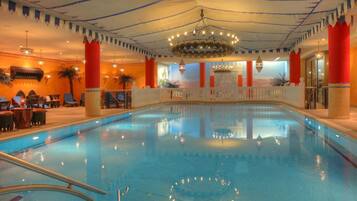 Una piscina interior con vista despejada al agua, un candelabro central y un área de descanso con mesas y sillas.