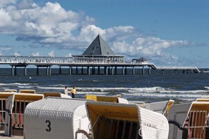 A pier with a triangular building at the end, beach chairs, and a view of the ocean.
