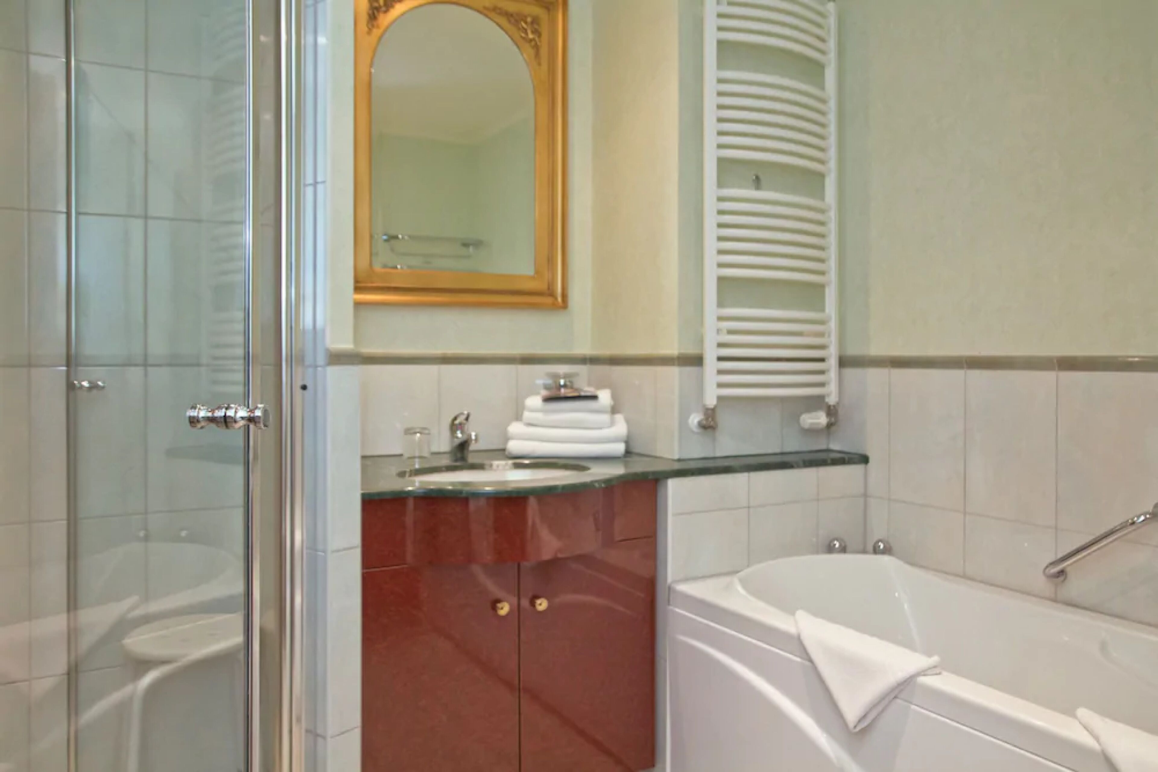 Une salle de bain dotée d’une douche à parois de verre, d’une baignoire blanche et d’un plan de toilette en verre avec un lavabo et une pile d’essuie-mains.