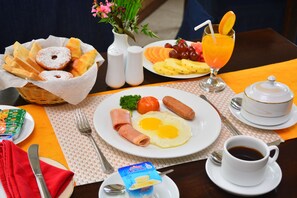 A breakfast table with various food items, including eggs, sausages, and a fruit plate. - Unique Cottages (Nuwara Eliya)