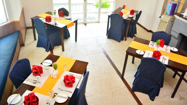 A dining area with tables set for four, blue chairs, and yellow table runners. - Unique Cottages (Nuwara Eliya)