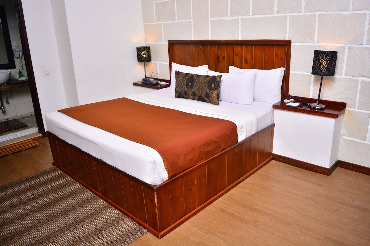 A wooden bed with white bedding, two bedside tables with lamps, and a stone wall.