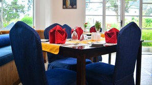 A dining area with a table set for four, blue upholstered chairs, and a yellow tablecloth. - Unique Cottages (Nuwara Eliya)