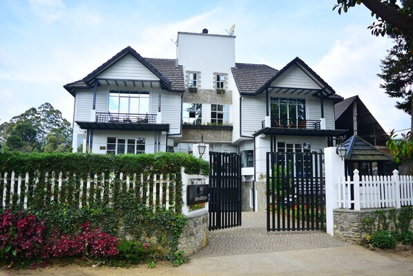 A two-story house with a white exterior, a stone facade, and a black gate. - Unique Cottages (Nuwara Eliya)