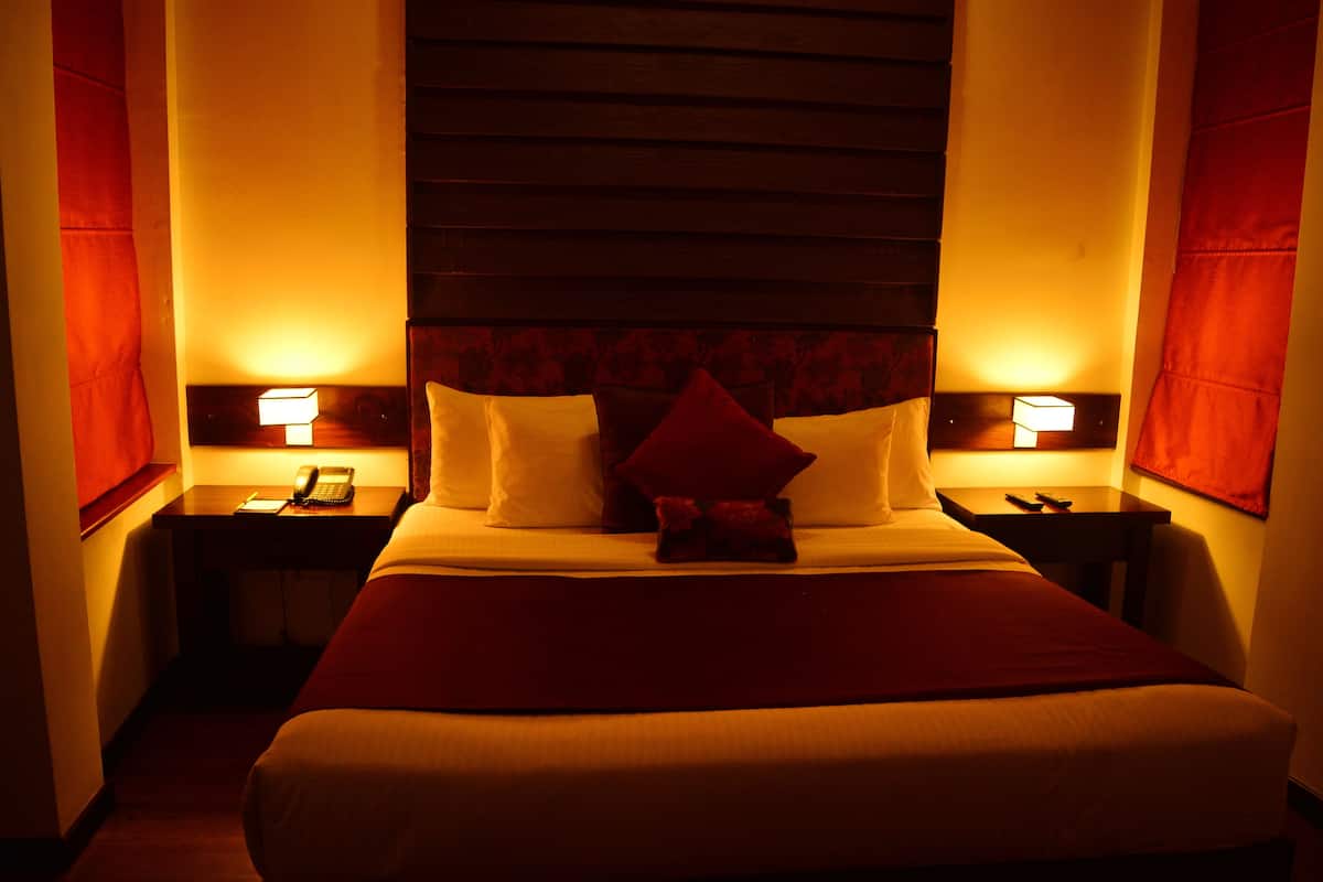 A hotel room with a large bed, two bedside tables with lamps, and a headboard with a patterned design.