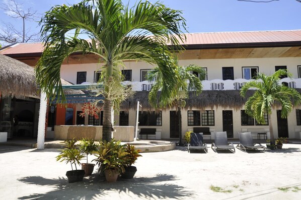A courtyard with palm trees, lounge chairs, and a building with a thatched roof.