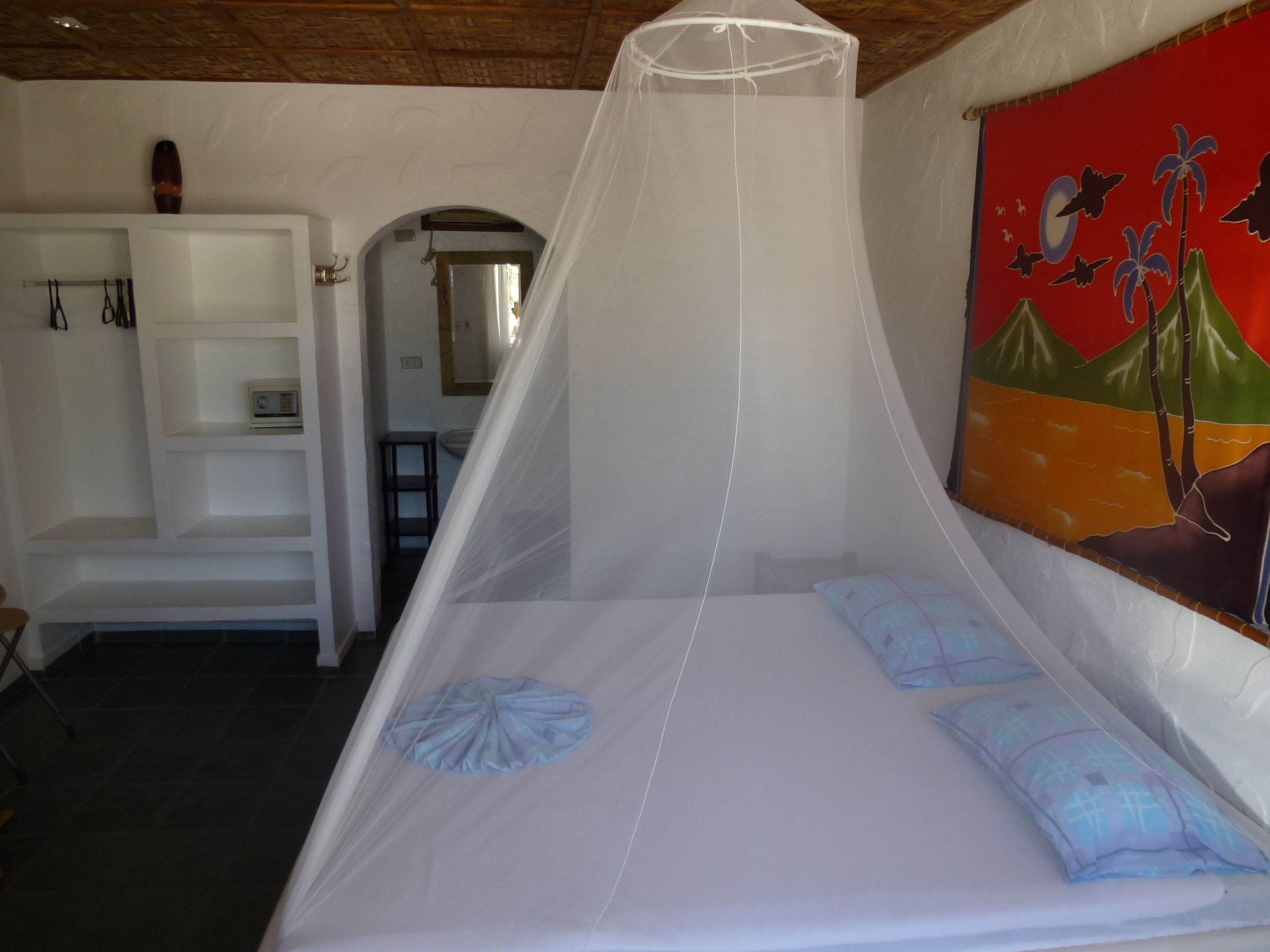 A single bed with a mosquito net, a white wardrobe, and a mural on the wall.