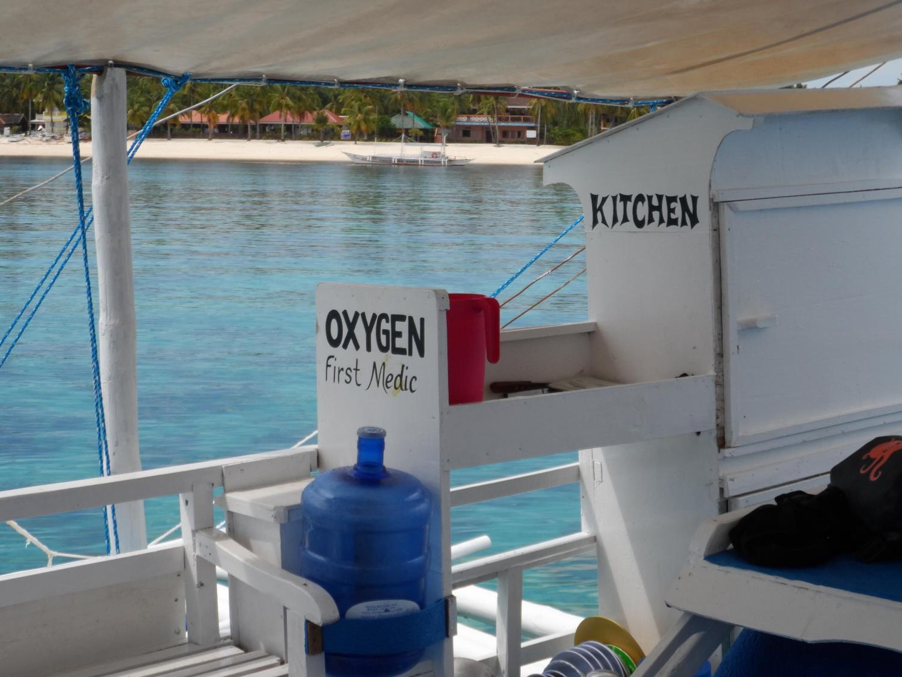 A boat's kitchen area with a sign labeled "OXYGEN First Medic" and a large blue oxygen cylinder.