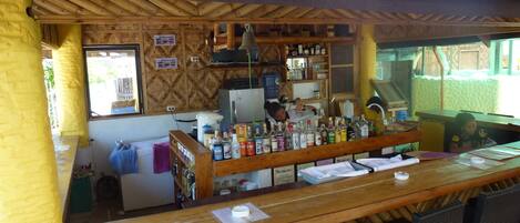 A bar area with a wooden counter, bar stools, and a refrigerator.