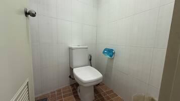 Un baño pequeño y limpio con azulejos blancos, un inodoro blanco, un dispensador de jabón azul y un cubo de basura.