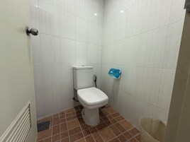 Un baño pequeño y limpio con azulejos blancos, un inodoro blanco, un dispensador de jabón azul y un cubo de basura.
