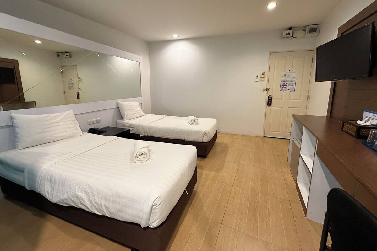 A hotel room with two beds, a desk, a television, and a mirror.