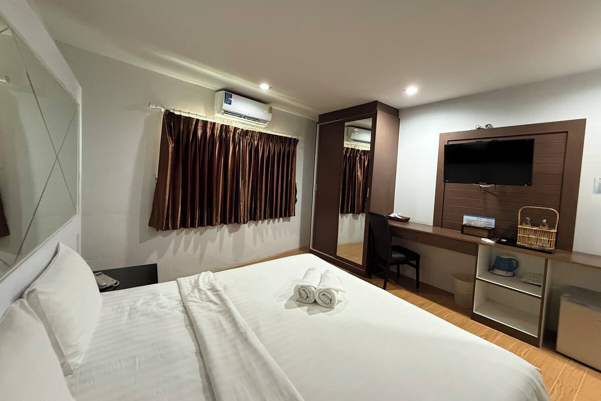 A hotel room with a bed, a desk with a chair, a TV, and a mirror.
