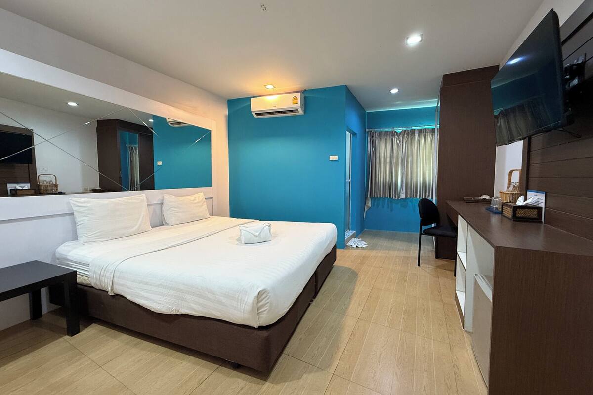 A hotel room with a bed, a desk, a chair, a TV, and a window with curtains.