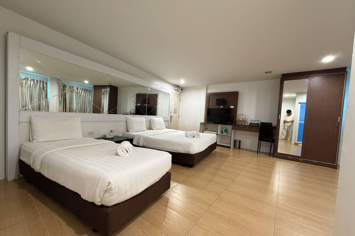 A hotel room with two beds, a desk, a TV, and a large mirror.