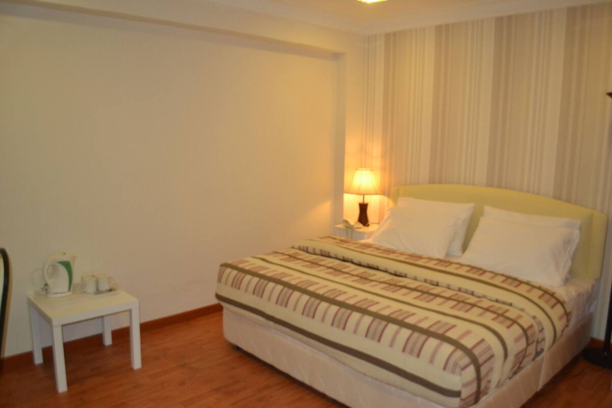A bedroom with a bed, bedside table, lamp, and a chair.