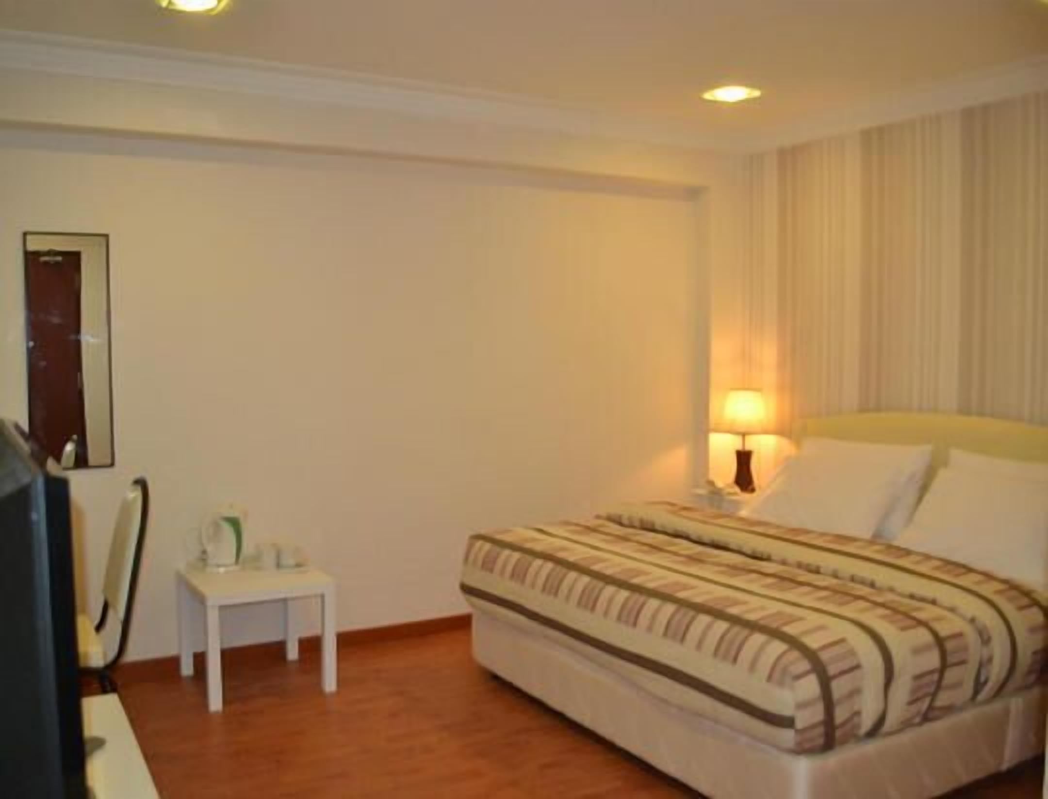 A hotel room with a bed, a bedside table, a lamp, and a mirror.
