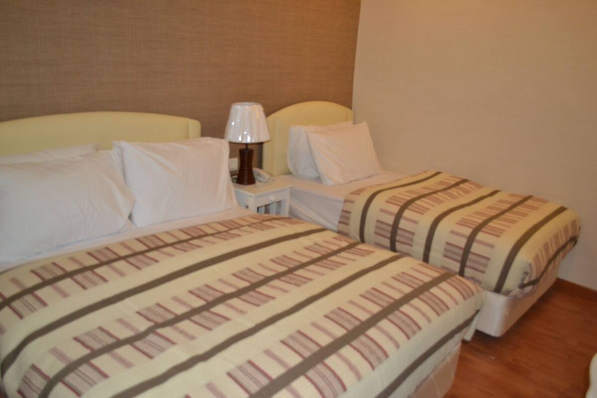 A hotel room with two beds, a nightstand, and a lamp.